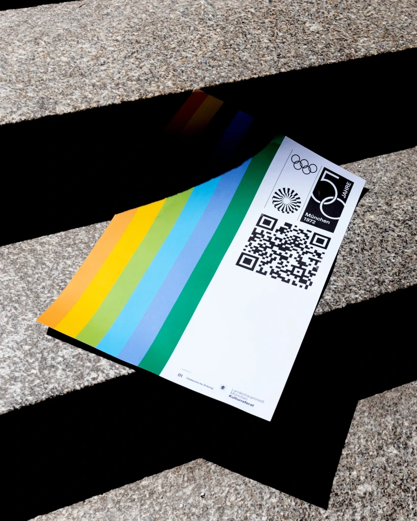 Auf einer Steintreppe liegt ein Flyer des 50-jährigen Jubiläums der Olympischen Spiele in München mit bunten Streifen