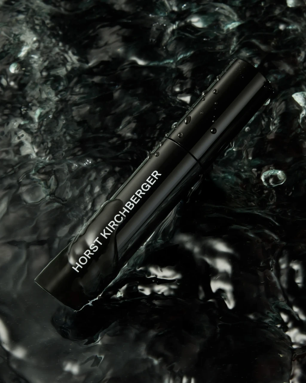 Eine schwarze Mascara der Marke Horst Kirchberger liegt halb eingetaucht in dunklem bewegten Wasser