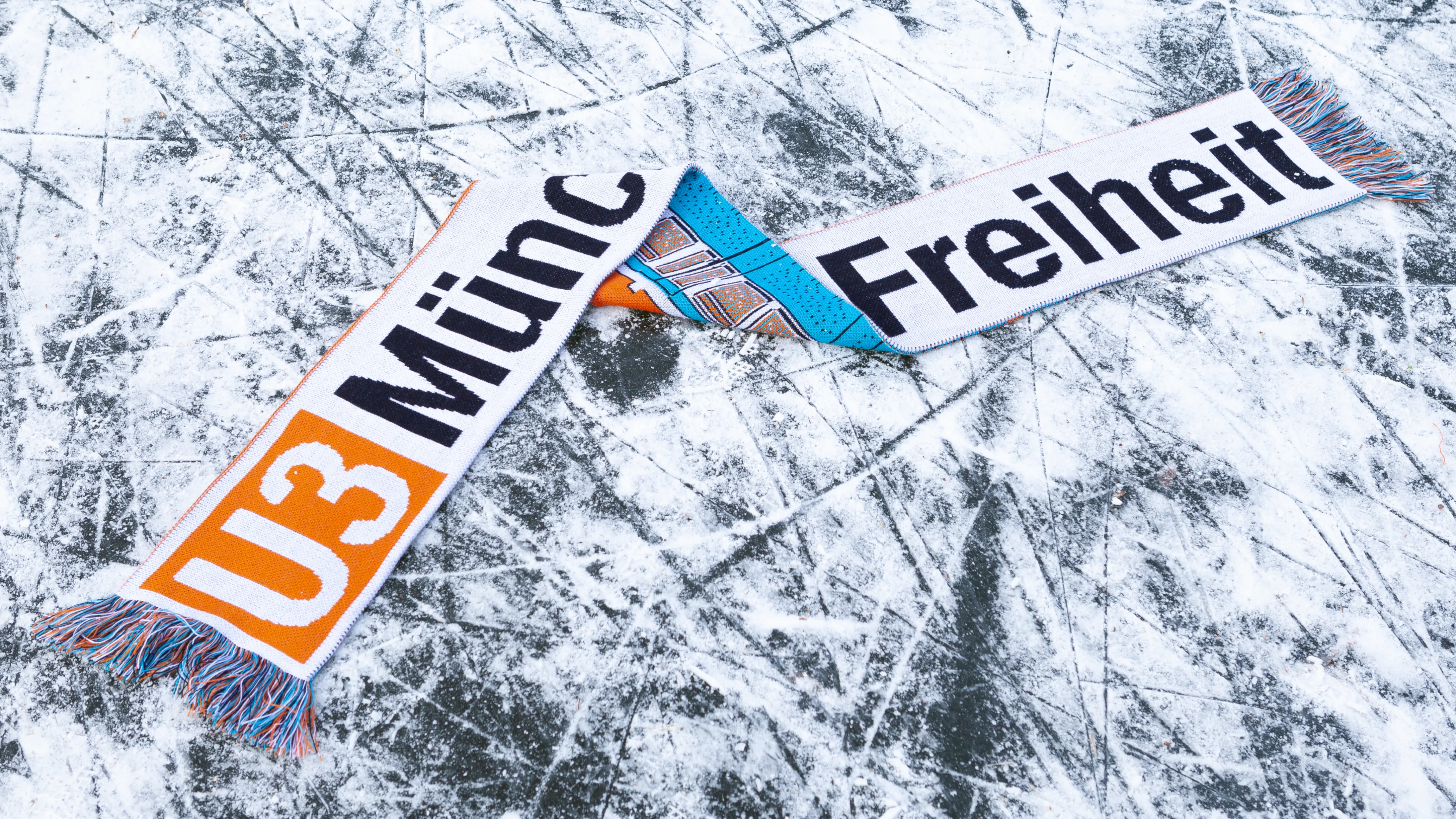Fußballlschal, der auf zugrfrorenem Kanal liegt. In U-Bahn Design der Schriftzug "U3 Münchener Freiheit"