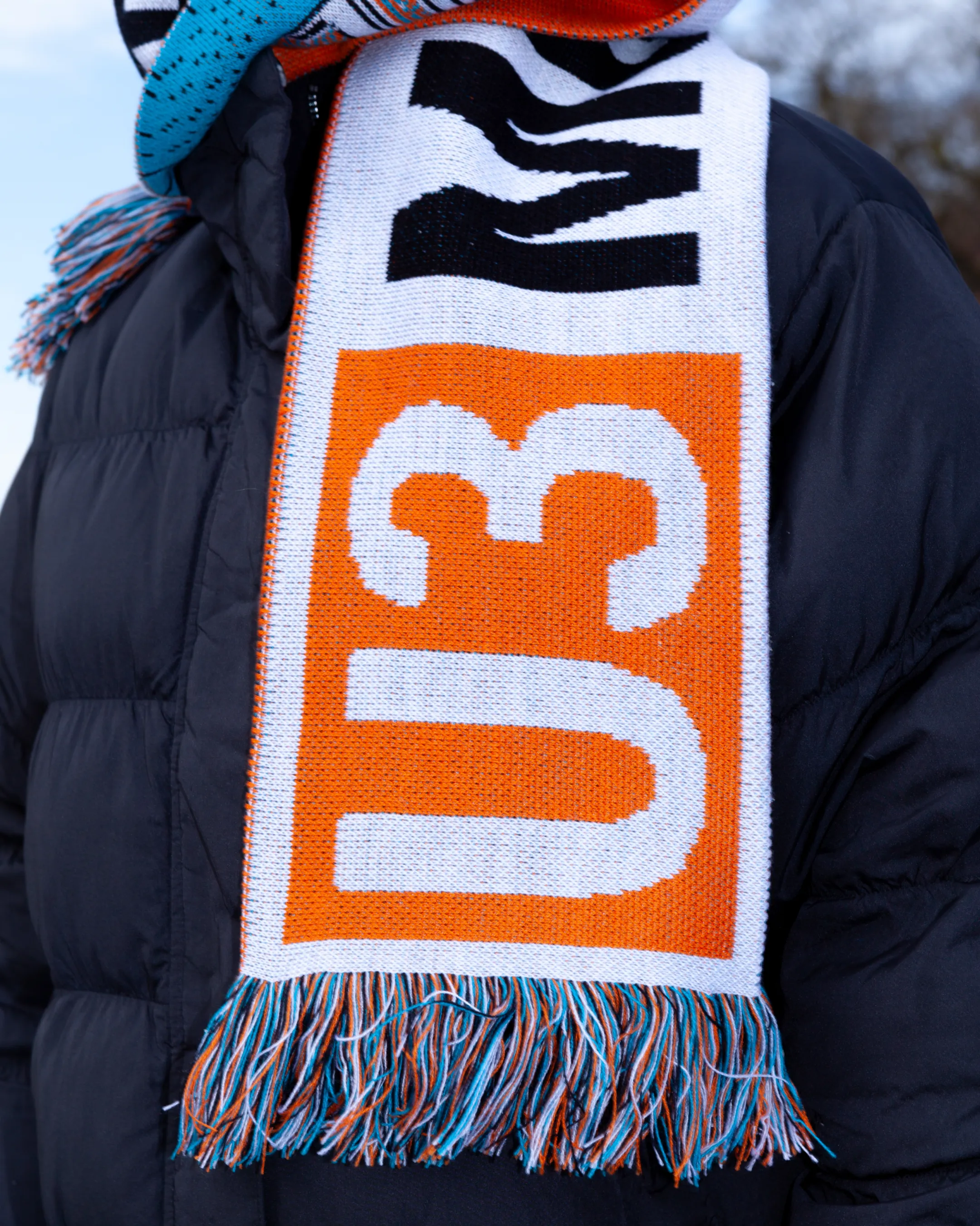 Deteilaufnahme des Fußballschals am Hals einer Person, im Fokus das weiße "U3" auf orangem Hintergrund