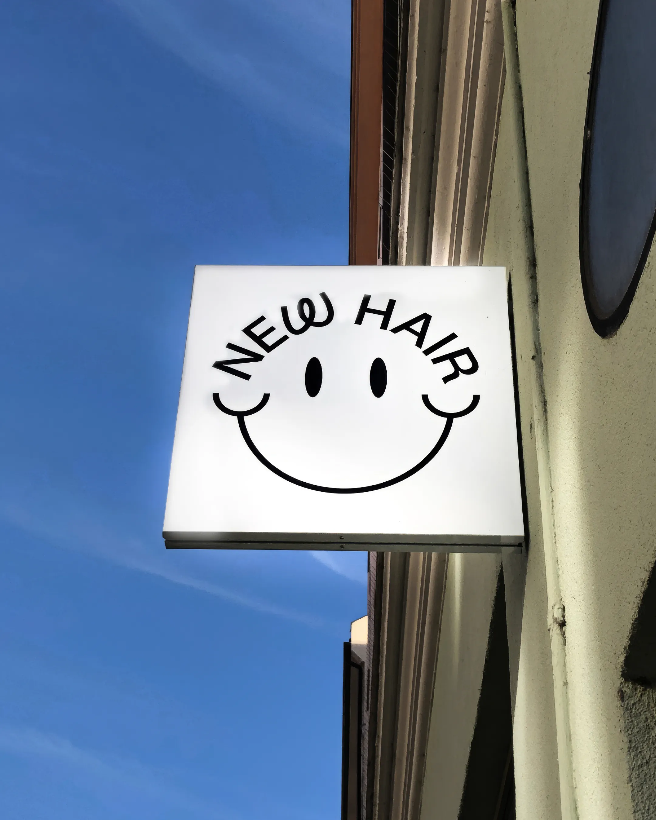 Ausleger-Schild / Nasenschild mit dem New Hair Logo, im Hintergrund blauer Himmel