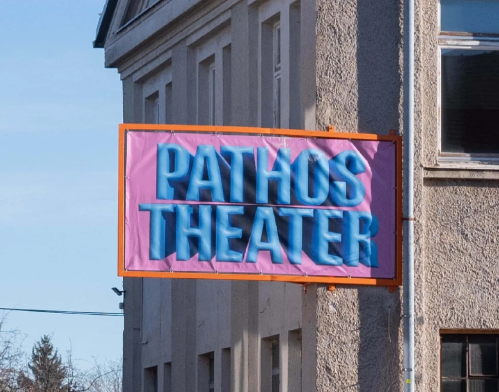 Gebäudebschilderung des Pathos Theaters. Blauer aufgeblasener 3D-Schriftzug auf pinkem Hintergrund und Orangener Rahmen