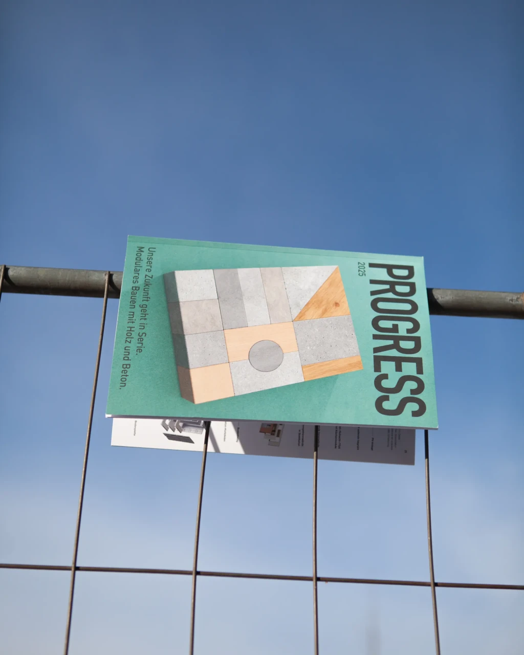 Strabag Progress Magazin hängt an einem Bauzaun vor einem blauen Himmel
