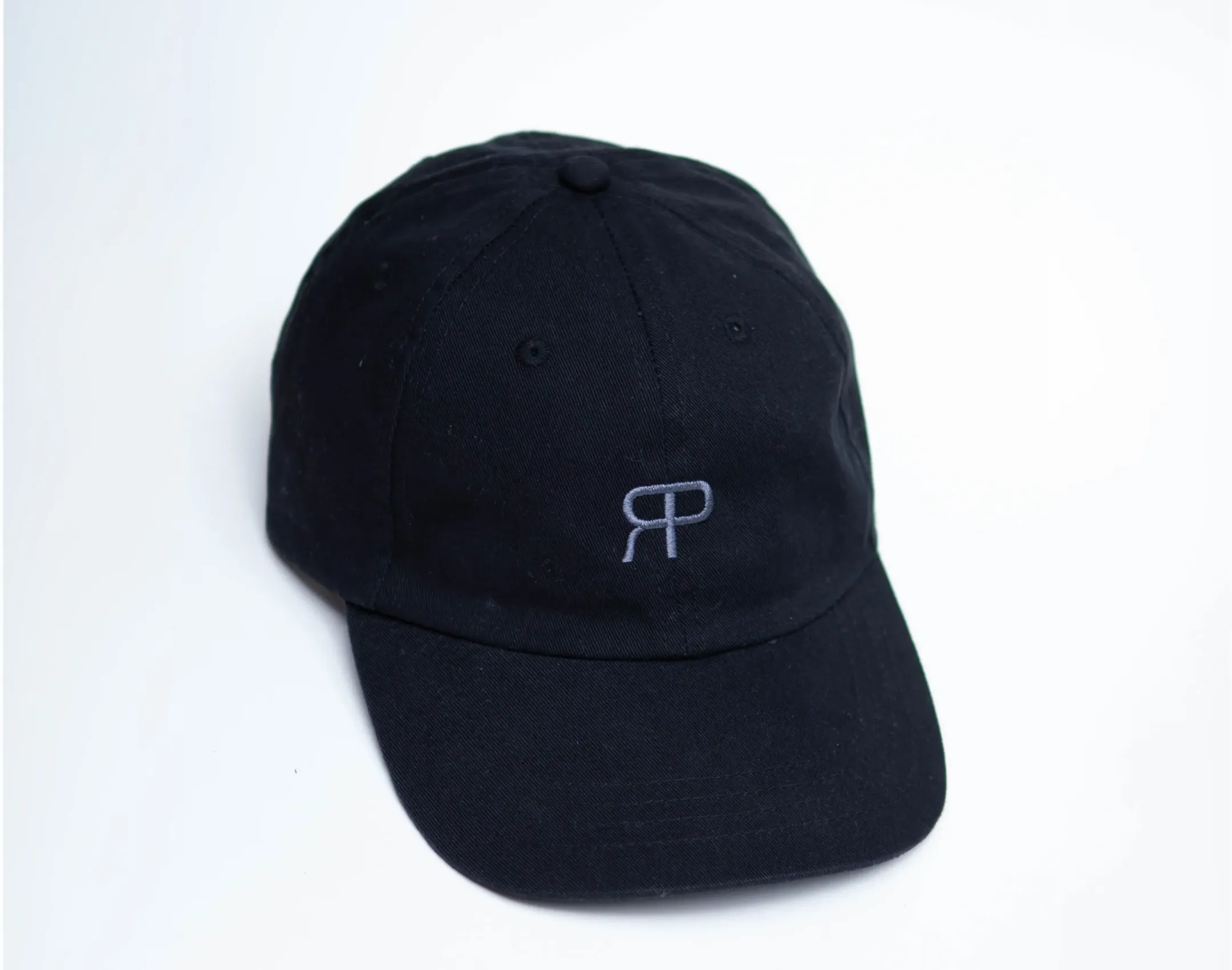 schwarze Merch Cap mit silber besticktem Rose Pistola Logo vor weißem Hintergrund